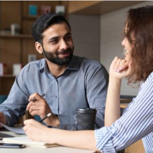 Indian male speaking with brunette female while sitting at a table.