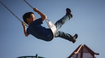 A young boy swinging on a swing against a blue sky.