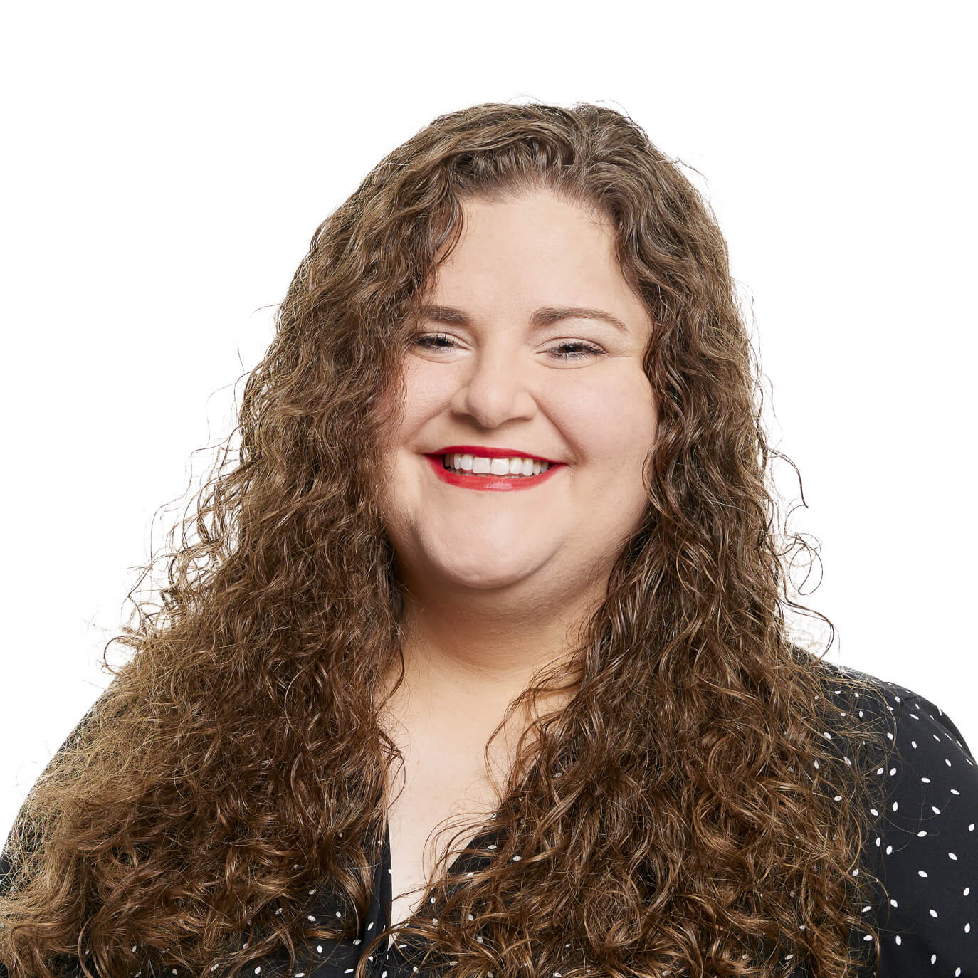 Woman with long, curly, light brown hair and black polka dot top smiling.