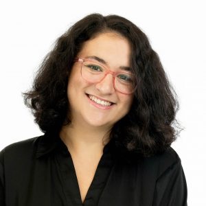 Woman with dark brunette hair in pink glasses and black top smiling.