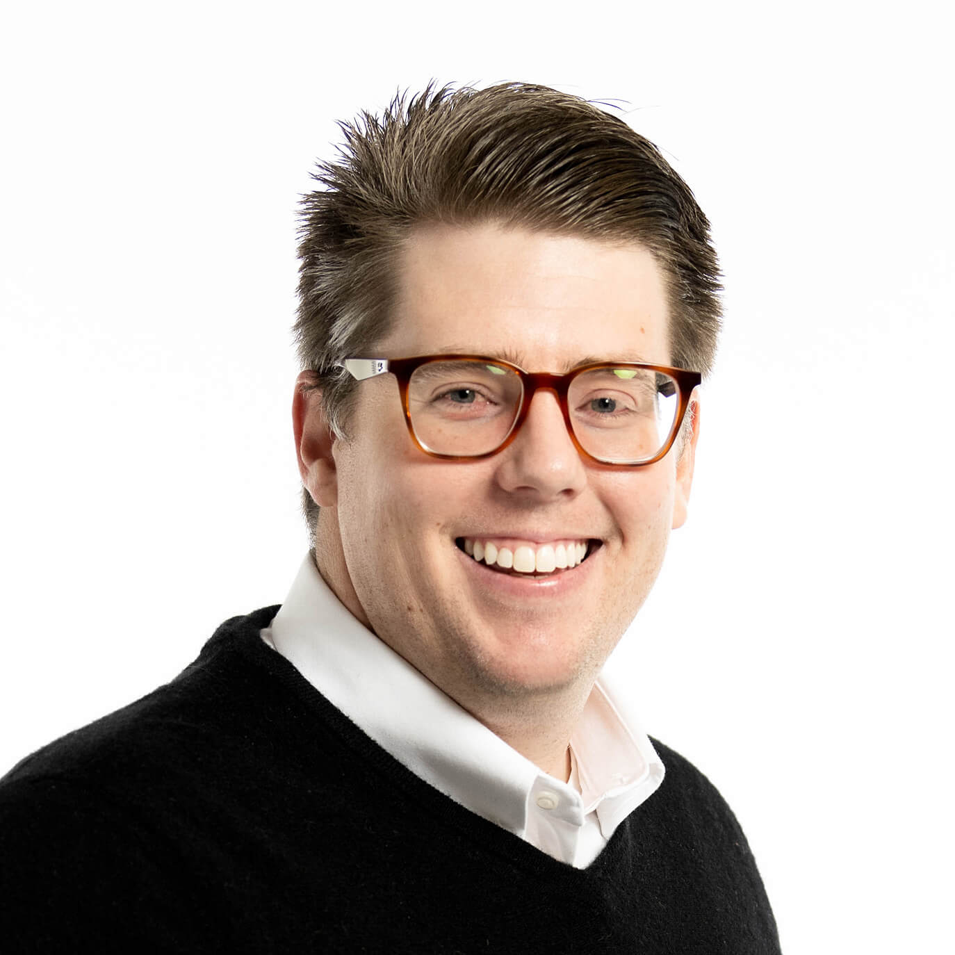 Brunette mail in white collared shirt, black vest, and reddish-brown glasses smiling.