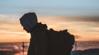 Photo of person walking along the beach wearing a hoodie and looking down.