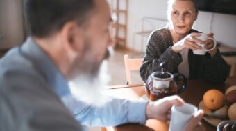 Photo of man and woman looking contemplative and sitting at a table drinking from mugs.