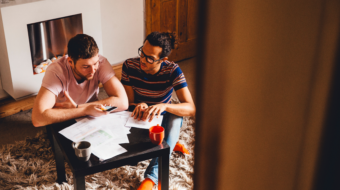 Photo of 2 people sitting on the floor around a table covered in papers.