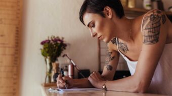 Woman with tattoos writing notes while leaning on counter