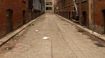 Photo of alley between brick buildings with litter and debris on the ground