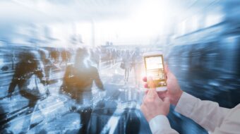 A picture containing person holding phone, blurred people walking through building