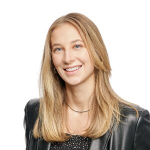 Kara Krnacik, with blonde hair and blue eyes, wearing a black leather jacket over a black polka dot blouse. Kara is smiling and has a nose ring and earrings.