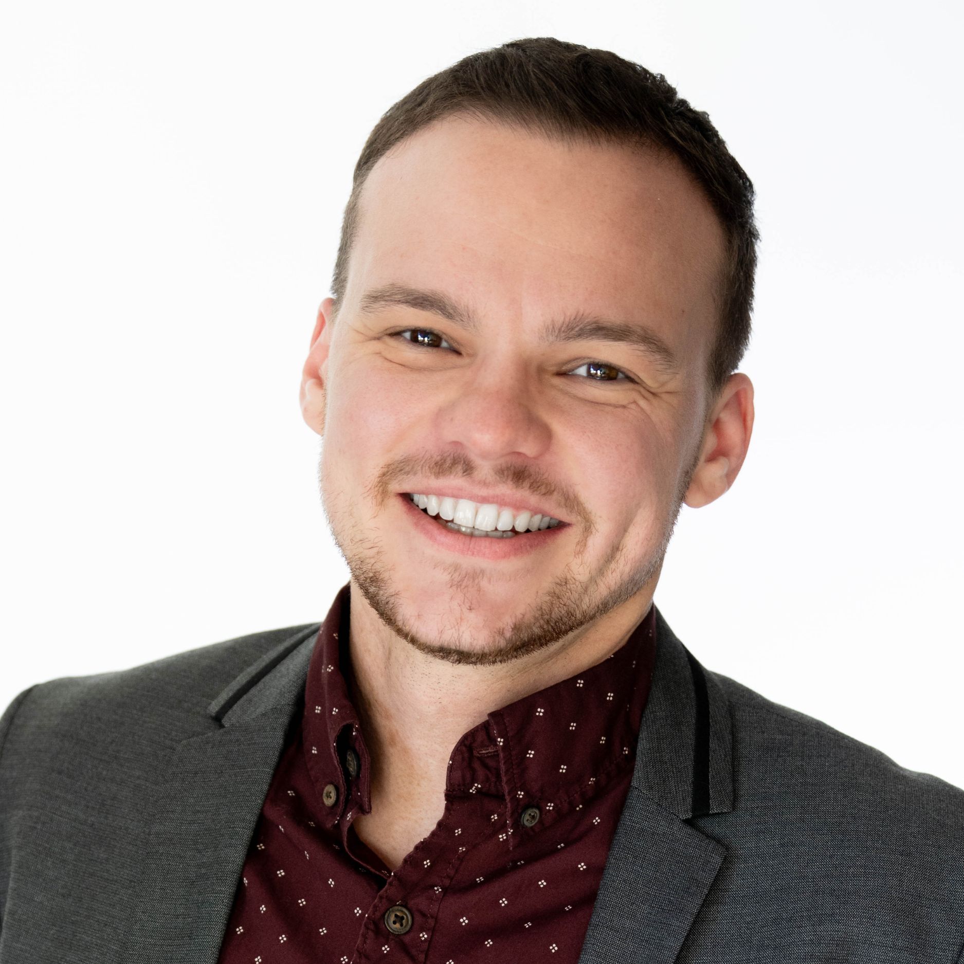 Man with short hair and smiling wearing a deep red patterned shirt and gray blazer