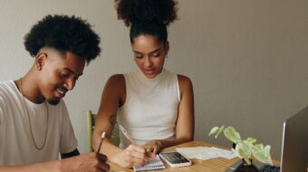 Black man and woman couple sitting at a table in front of a laptop doing personal finances. They look happy and hopeful.